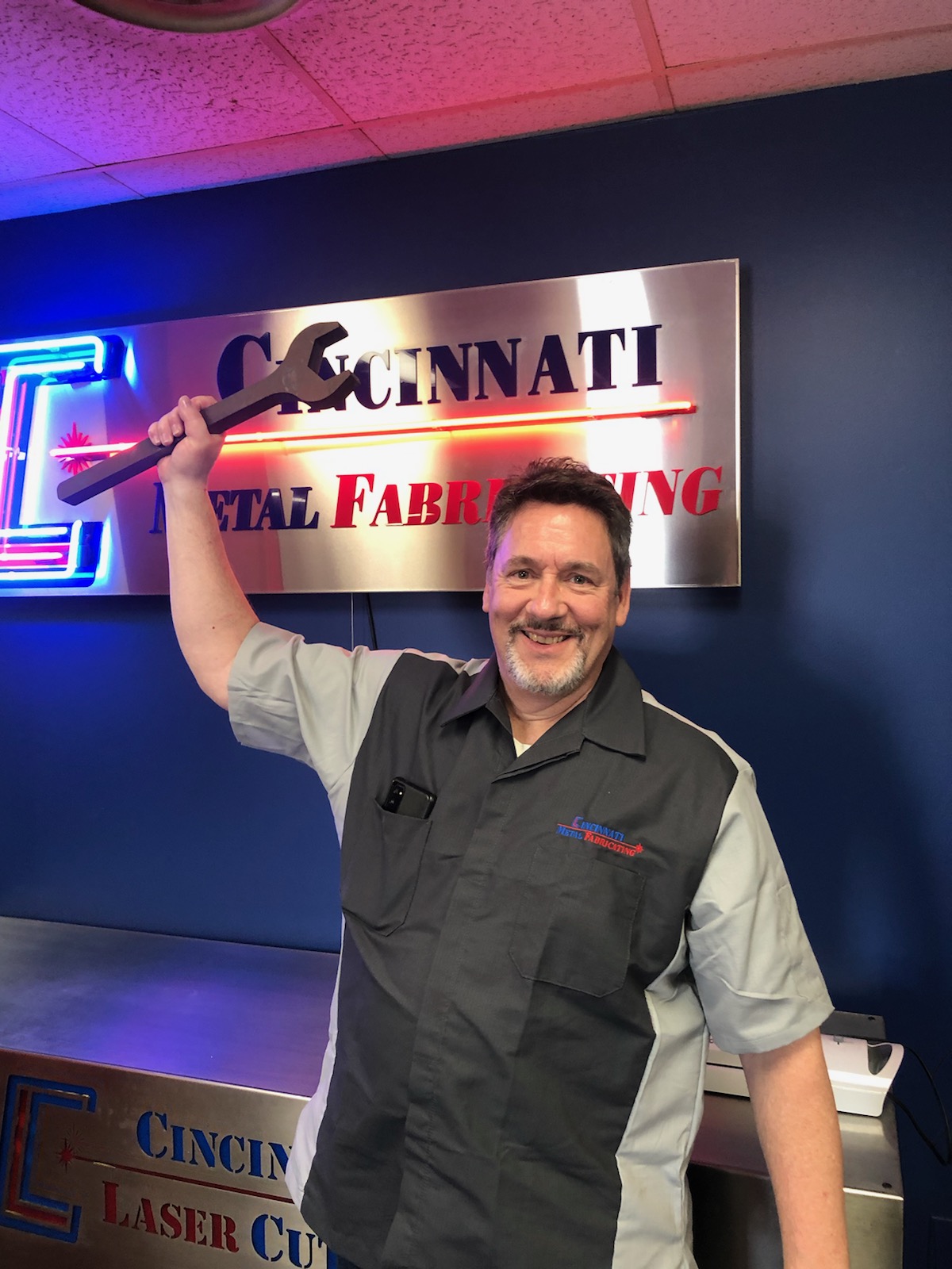 CMF team member holding custom fabricated wrench by Cincinnati Metal Fabricating sign